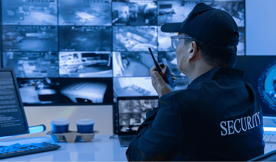 Security officer monitoring multiple CCTV screens, holding radio